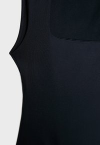 Svart ärmlös topp i slät tyg, med rundad halsringning och detaljer med en rektangulär bakficka.