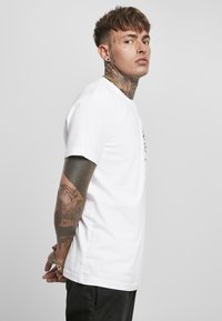 White short-sleeve t-shirt featuring a crew neck, smooth texture, and a simple design. Worn with dark pants, minimalistic style.