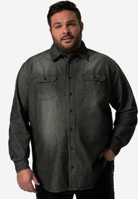Camicia di denim nera con maniche lunghe, chiusura con bottoni, due tasche sul petto e colletto. Presenta una finitura testurizzata, leggermente sbiadita.