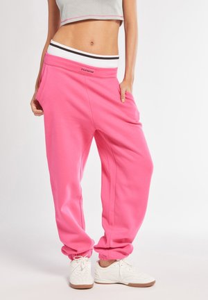 Pantaloni sportivi rosa con una vestibilità rilassata, vita ampia con strisce bianche e nere e tasche laterali. Tessuto morbido con polsini a costine.