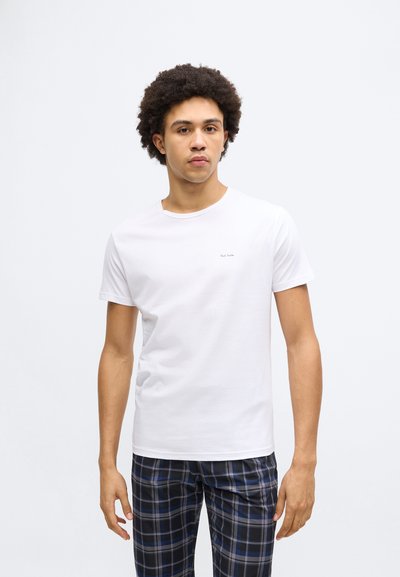 Tricou alb din bumbac cu decolteu rotund, mâneci scurte, având un mic detaliu cu text de marcă pe partea din față. Purtat cu pantaloni de pijama în carouri.