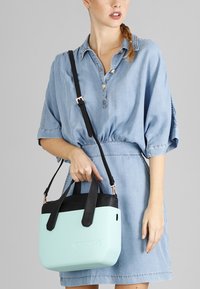Una borsa a mano verde menta con finitura testurizzata, dettagli in pelle nera e doppi manici. Dotata di una tracolla removibile.