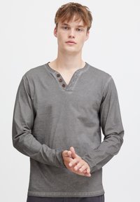 Langärmliges graues Shirt mit V-Ausschnitt, braunen Knöpfen und weicher Textur. Es bietet eine lässige Passform und minimalistische Designdetails.