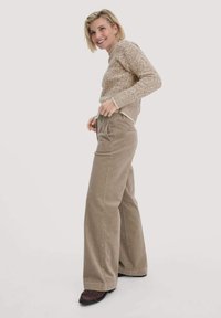 Beige gebreide trui met een textuurpatroon, gecombineerd met lichtbruine corduroy wijde broek. Donkere schoenen met een franjerand.