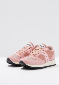 Paire de baskets en daim rose et mesh avec des semelles intermédiaires blanches et des semelles extérieures texturées noires, arborant le logo Saucony sur les languettes et les côtés.