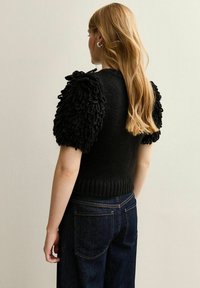 Top nero lavorato a maglia con maniche a sbuffo in tessuto testurizzato e fluffoso. Presenta una vita aderente a coste, abbinato a jeans dritti blu scuri.