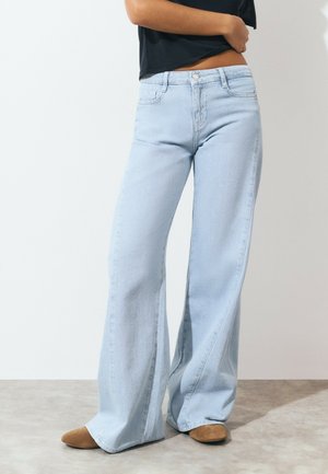 Jean large bleu clair en denim avec un design classique à cinq poches et une fermeture à bouton. Texture lisse et ourlet à longueur de sol.