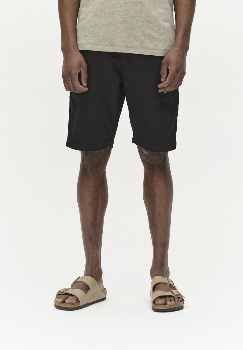 Pantalones cortos negros con un corte relajado, material de algodón, dobladillo vuelto. Combinados con sandalias planas de color beige claro con correas ajustables.