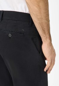 Schwarze Baumwoll-Chambray-Hosen mit Knopfverschluss, seitlichen Taschen und einer Gesäßtasche. Glatte Textur mit sichtbaren Stitching-Details.