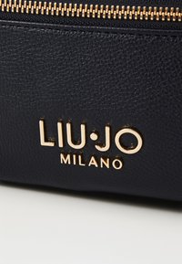 Zwarte textuurleren tas met een gouden ritssluiting en het ingedrukte logo "LIU·JO MILANO" op de voorkant. Elegant en minimalistisch ontwerp.