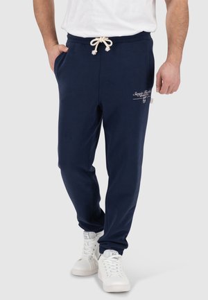 Navy jogger pants made from cotton blend material. Features elastic waistband with drawstring, side pockets, and logo detailing.