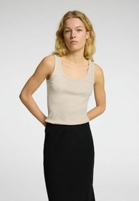 Lichtbeige geribbelde tanktop met een ronde halslijn, gecombineerd met een lange zwarte rok. De stof lijkt zacht en lichtjes gestructureerd.