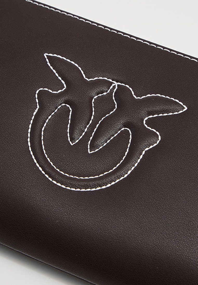 Superficie in pelle marrone scuro con un motivo in rilievo e cuciture bianche raffigurante due uccelli che si fronteggiano in un disegno circolare.