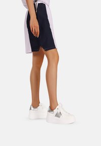 Sneakers bianchi con dettagli in argento, design con lacci e pannello testurizzato. Abbinate a pantaloni corti blu navy e lilla chiaro.