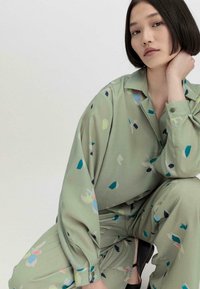 Grünes Blusen- und Hosen-Set aus leichtem Stoff mit abstrakten Pastellmustern in Blau, Pink und Weiß; lockere Passform und knöpfbare Bündchen.