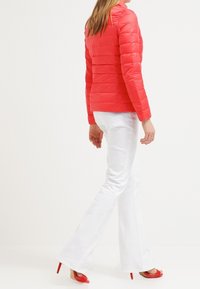 Röd vadderad jacka med horisontellt quiltad design, uppstående krage och slim fit. Stor matchande med vita utsvängda jeans och röda klacksandaler.