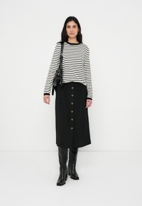 Ριγέ μακρυμάνικο τοπ σε ασπρόμαυρο, σε συνδυασμό με μαύρη μίντι φούστα με κουμπιά μπροστά και μαύρες μπότες μέχρι το γόνατο.