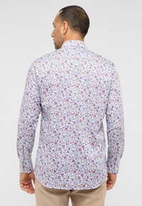 Langarmshirt met een witte basis en een multikleurig bloemenpatroon. Soepele stof met een kraag met knopen en een gebogen onderrand.
