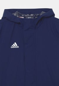 Veste à capuche bleu marine en tissu doux avec une texture lisse ; présente le logo Adidas blanc sur la poitrine gauche. Design minimaliste.