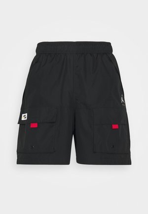 Shorts cargo noirs avec taille élastique, deux poches avant à rabat avec des onglets rouges, et un petit logo blanc sur le côté droit.