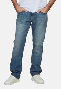 Jeans de mezclilla azul claro con un corte recto, diseño de cinco bolsillos y costuras contrastantes, combinados con zapatillas blancas.