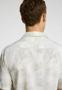 Kortærmet skjorte i hvidt stof med et subtilt ginkgo-blad mønster. Har en camp krave; glat tekstur, letvægtsdesign.
