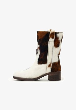 Leren laars van koeienhuid tot halverwege de kuit met bruine, zwarte en witte vlekken, een lage blokhak en aantreklussen aan de zijkant.
