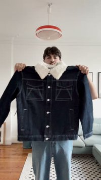 Temno modra denim jakna z belim umetnim krznom okoli ovratnika, zapenjanjem na gumb in dvema žepoma na prsih. Ima kontrastne šive in sproščen kroj.