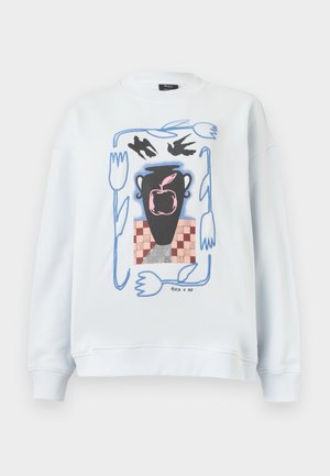 Witte sweater met een afbeelding van een zwarte vaas waarin een roze appel ligt, twee zwarte vogels erboven, omringd door blauwe abstracte bloemen en een dambordpatroon.