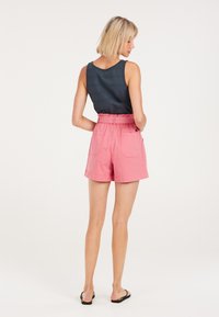 Pantaloni shorts di cotone rosa con vita elastica, tasche laterali e una vestibilità comoda, abbinati a un top senza maniche blu scuro.