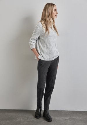 Maglione grigio chiaro a coste con una vestibilità ampia e scollatura a girocollo, abbinato a pantaloni sartoriali grigio scuro e ankle boots neri.
