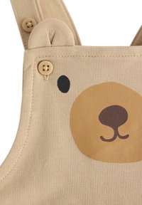 Beige tuinbroeken hebben een ontwerp met een berengezicht, met een bruine neus en oren. Houten knopen bevestigen de banden, met een zachte, gestructureerde katoenstof.