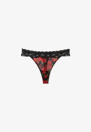 Tanga negra con borde de encaje que presenta un patrón floral en rojo y verde sobre un fondo negro translúcido. Los delicados bordes en forma de onda realzan el diseño.