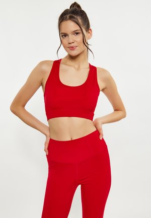 Rød sports-BH med scoop-udskæring og samlet stof i taljen, parret med højtaljede røde leggings, begge lavet af strækbart stof.