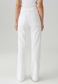 Jeans bianchi a vita alta con stile dritto, dotati di due tasche posteriori e un tessuto testurizzato. Hardware minimale visibile.