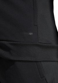 Pantaloni sportivi neri con una texture liscia, dotati di una vita elastica e di un logo "READY" discreto in finitura opaca sul tessuto.