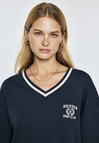Felpa navy a collo a V con bordo bianco a contrasto, con logo ricamato "BIGSTAR DNM CLUB" e vestibilità rilassata. Tessuto morbido.