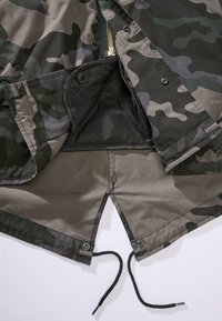 Jakke med camo-mønster i en mørkegrønn og grå fargekombinasjon. Har glidelås, knapper og snor i kanten. Jevn tekstur.