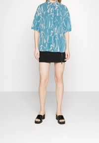 Camicia azzurra a maniche corte con motivi astratti bianchi, abbinata a una gonna nera aderente con cerniera laterale e sandali con zeppa neri.