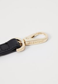 Musta nahkavyö, jossa on kultainen hummerilukko, jossa lukee "VALENTINO" kaiverrettuna, sileä pinta ja kiillotettu metallinen viimeistely.