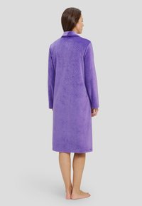 Bata de baño morada de manga larga, hecha de suave forro polar texturizado con un collar, que presenta un patrón de puntos y llega hasta la mitad de la pantorrilla.