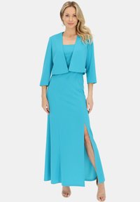 Turkusowa sukienka dwuczęściowa z dopasowanym gorsetem i spódnicą w kształcie litery A z bocznym rozcięciem, zestawiona z krótką kurtką z trzema ćwiartkami rękawów.