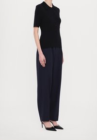 Czarna krótka bluzka dzianinowa z kołnierzykiem i guzikami, zestawiona z wysokimi granatowymi spodniami o szerokich nogawkach i czarnymi szpilkami z ostrym noskiem.