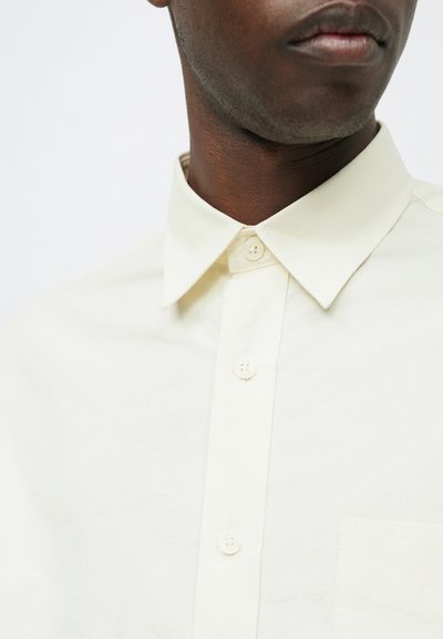 Jasnożółta koszula z kołnierzykiem rozpostartym, z kieszonką na lewym piersiu i gładką teksturą materiału.