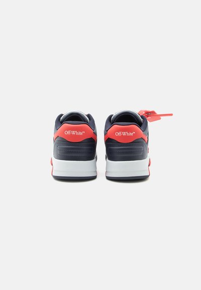 Een paar marineblauwe en rode Off-White sneakers gezien van achteren, met een rode zip tie bevestigd aan de rechter schoen.