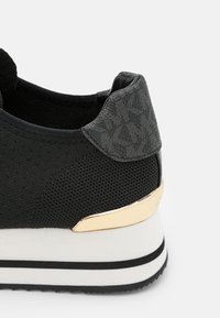 Svart sneakers med en strukturert grå hæl, gullaccent og en hvit såle med svarte striper. Materialet er mesh med en glatt overflate.