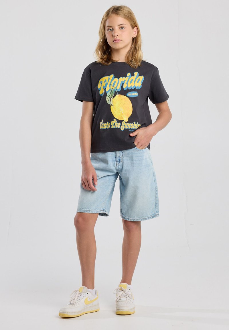 Schwarzes Grafik-T-Shirt mit "Florida" und einem gelben Zitronendruck. Kombiniert mit hellblauen Jeansshorts und weißen Sneakers mit gelben Akzenten.