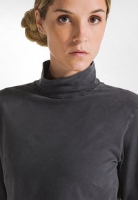 Donkergrijze, lange mouwen turtleneck met een soepele textuur. Het heeft een slim fit en een hoge kraag. Subtiele naden en geen zichtbare hardware of patronen.