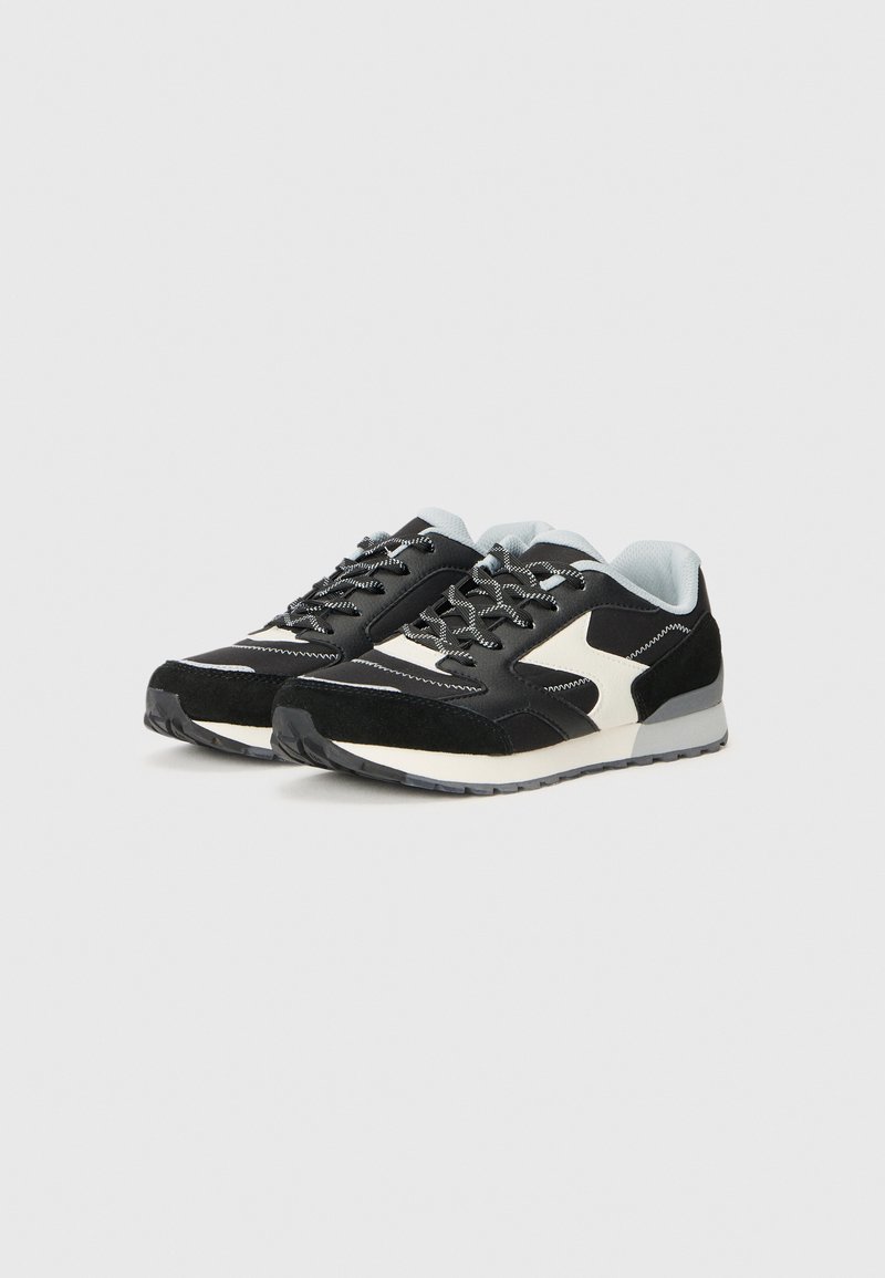 Schwarz-weiße Sneaker mit einem Obermaterial aus Wildleder und Mesh, Gummisohle und kontrastierenden Nähten. Verfügt über auffällige Schnürsenkel und einen gepolsterten Knöchelbereich.