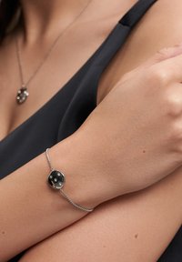 Bracciale in tono argento con un pendente rotondo e trasparente, impreziosito da tre piccole pietre, fissato con una sottile catena testurizzata.